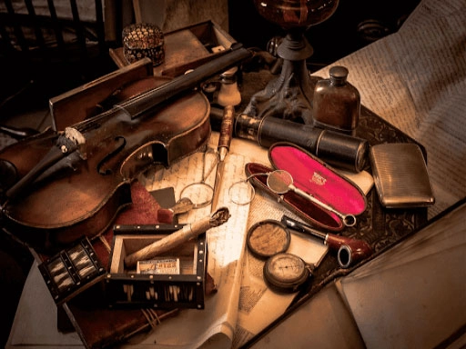 A vintage-themed assortment of items displayed on a wooden desk, including an old violin, a cigar box, magnifying glasses, a pipe, a compass, a telescope and a fountain pen.